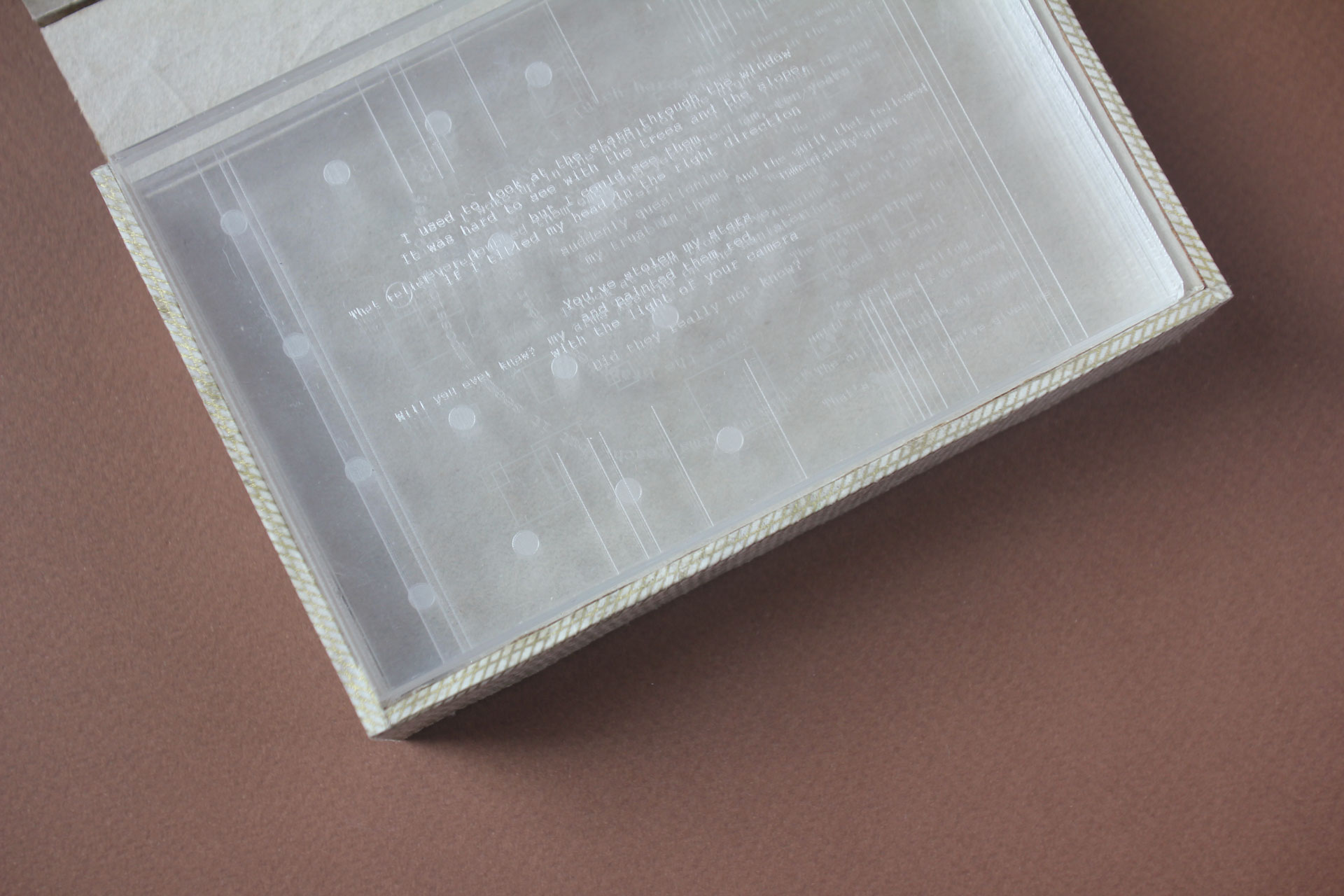 A close up shot of opened narrative object. Inside the box are acrylic panels that have etchings of differnt text and symbols from archived writing samples.